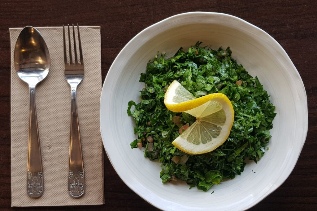Traditional Tabouli salad made with finely diced parsley, onion and tomato mixed in lemon and olive oil dressing with a dash of cous cous and lemon slice on top